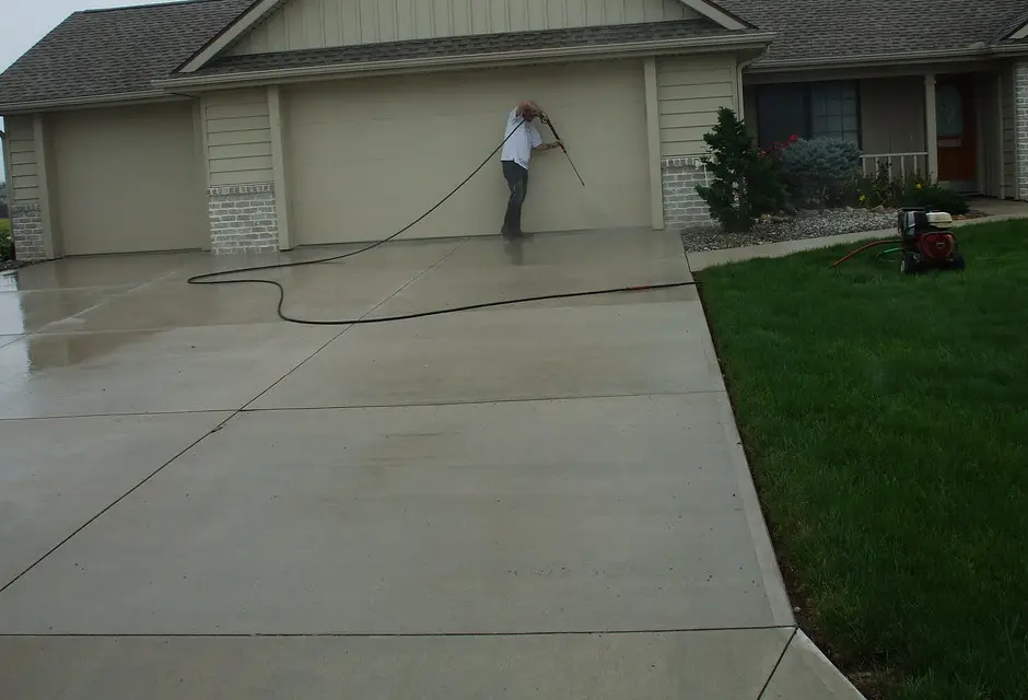 Pressure washing a concrete driveway in front of a three-car garage