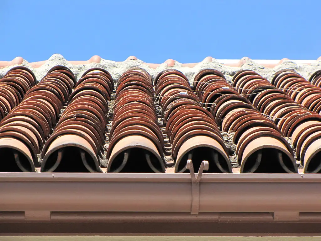 Close-up of a barrel tile roof edge with debris collecting in the tile openings